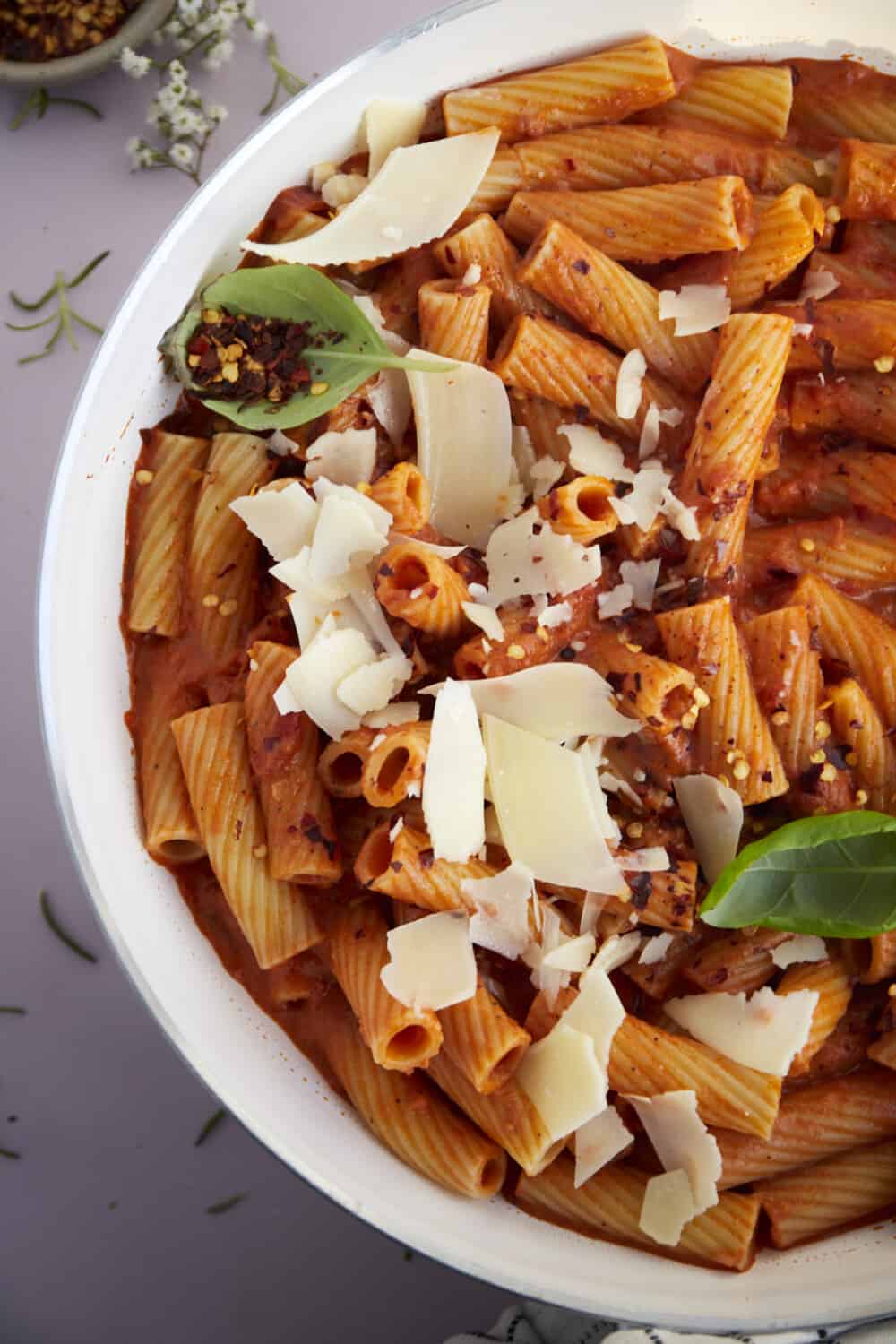 a bowl of spicy rigatoni pasta topped with shaved Parmesan and red pepper flakes.