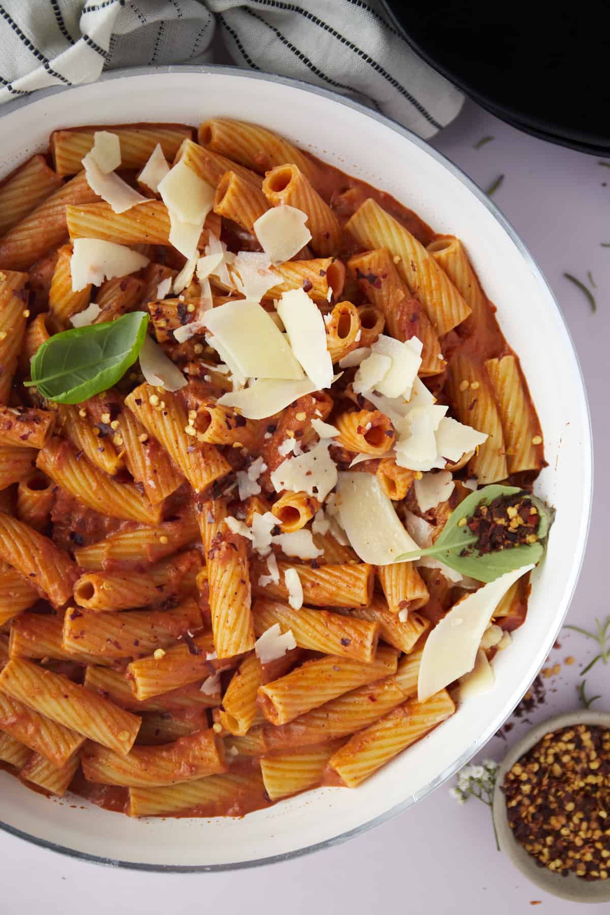 a bowl of spicy pasta topped with red pepper and shaved parmesan.