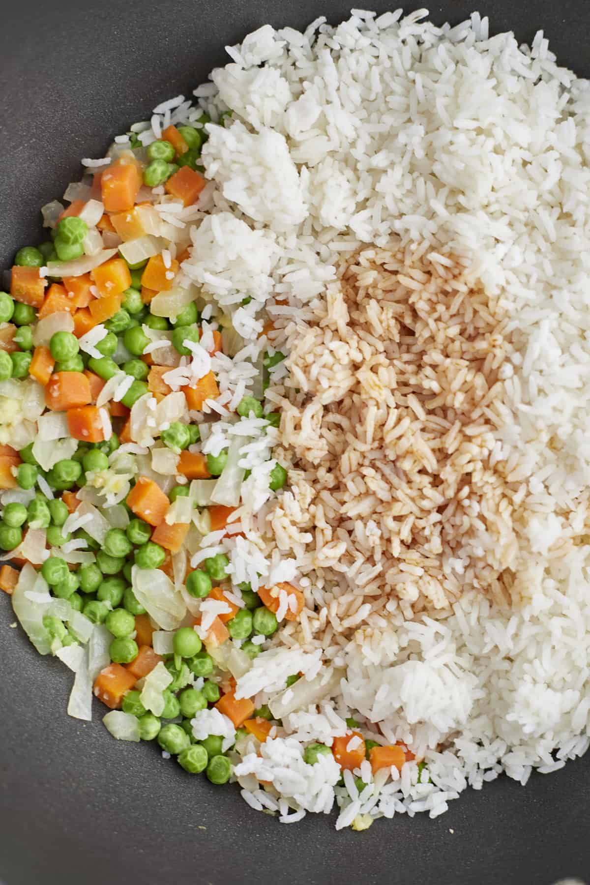 close up image of carrots, peas, onions, rice, and seasonings in a wok to make egg fried rice