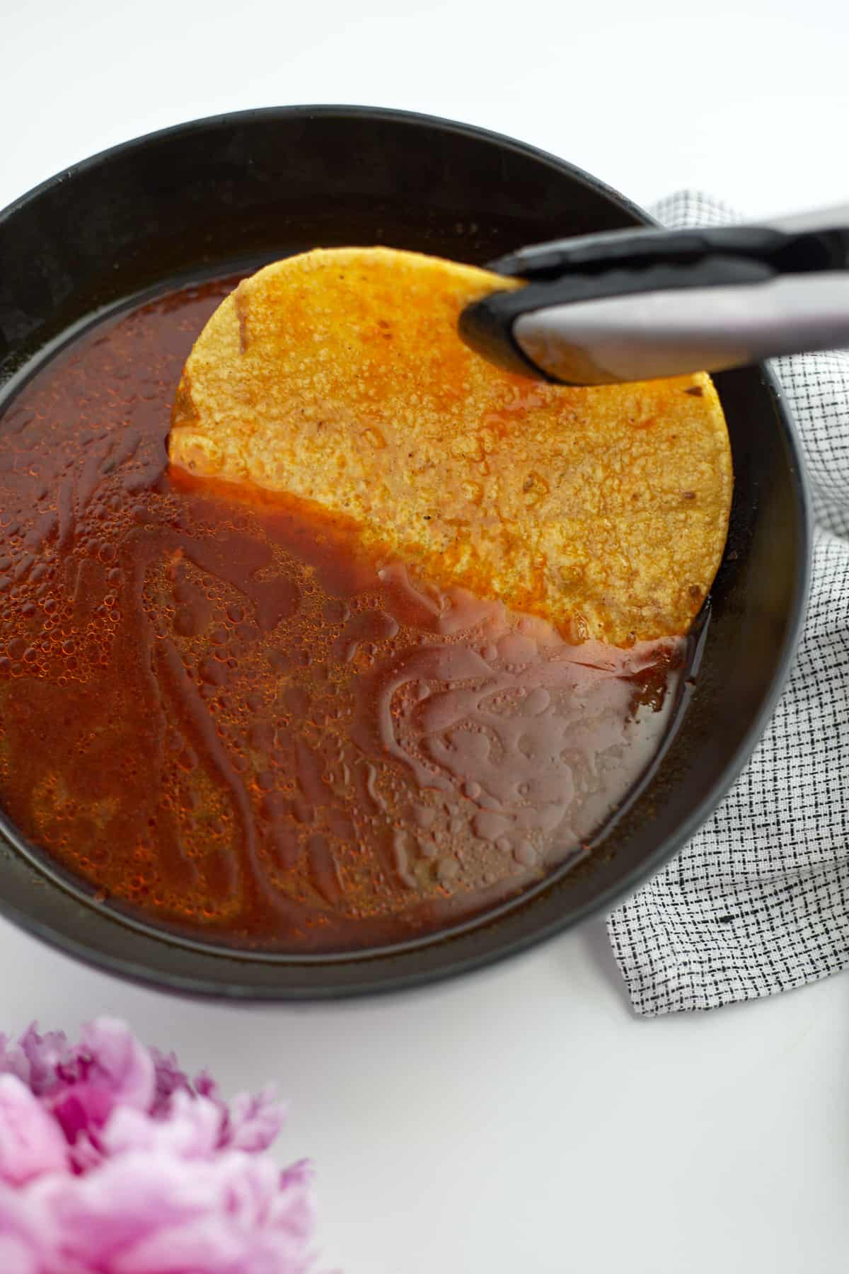 tongs dipping a corn tortilla into birria sauce