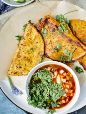 Slow Cooker Beef Birria tacos on a plate with a bowl of pico de gallo on the side