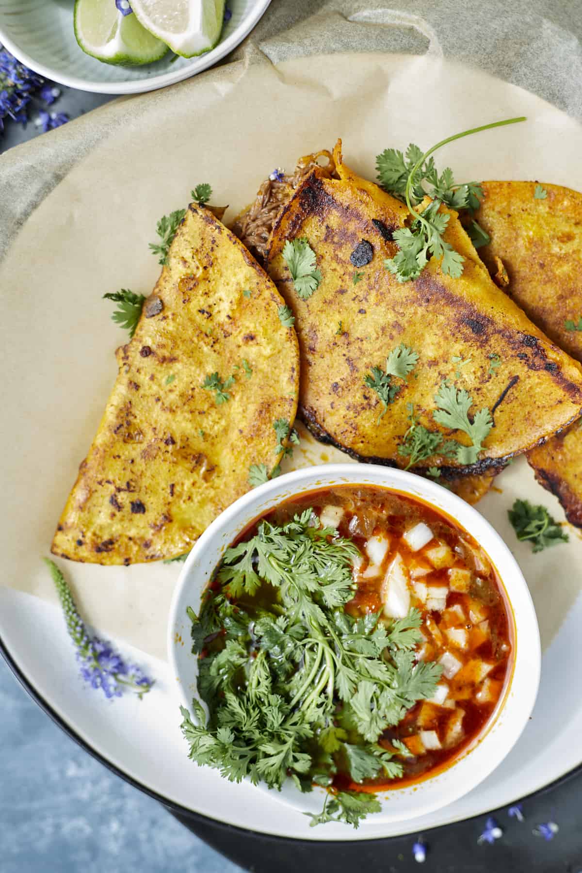 beef birria tacos on a platter with a small ramekin of extra sauce