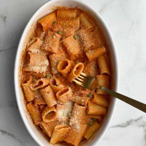 overhead image of baked rigatoni in a white dish topped with parmesan cheese with a fork spearing a noodle