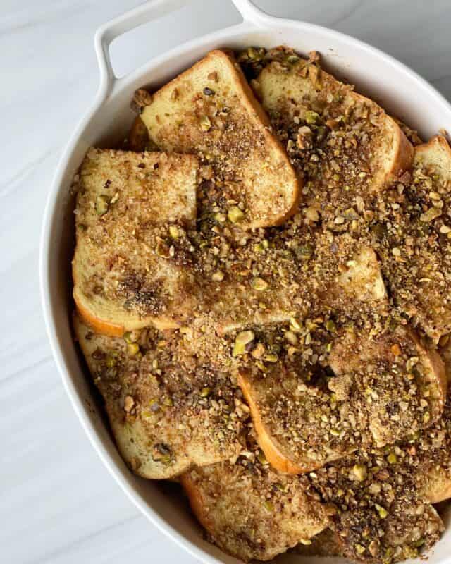 overhead image of baklava brioche french toast topped with nuts and cinnamon sugar in a white baking dish
