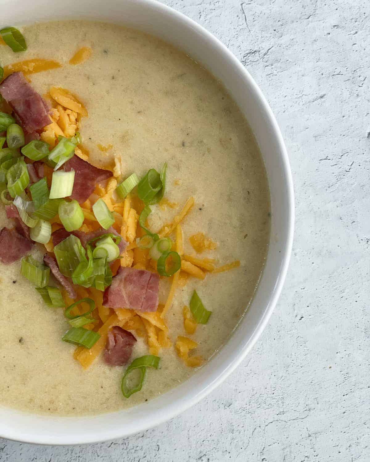 Crockpot potato soup topped with green onions, cheese, and bacon