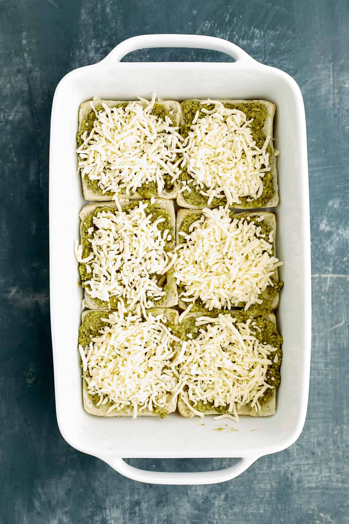sliced bread in a baking dish topped with pesto and cheese.