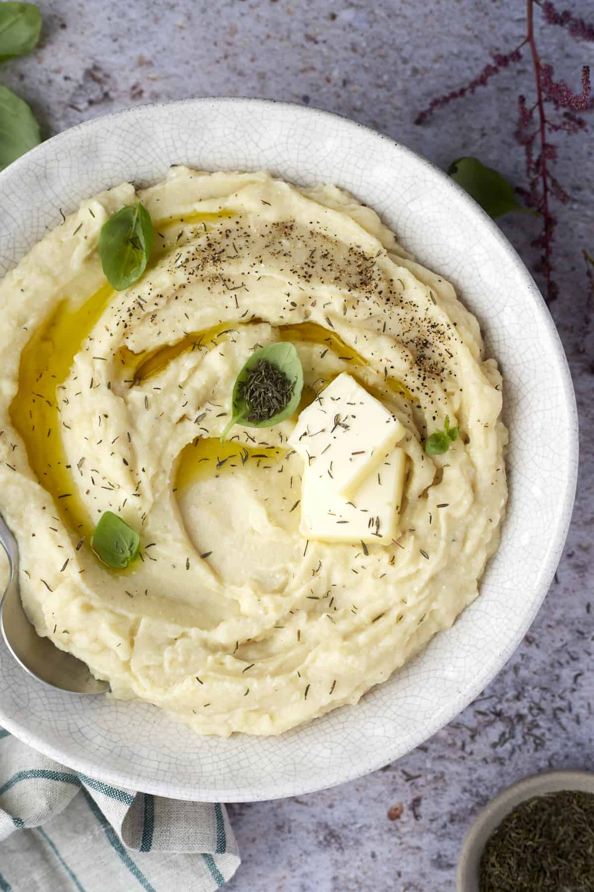 a bowl of baked cheesy mashed potatoes topped with a pad of butter and fresh herbs