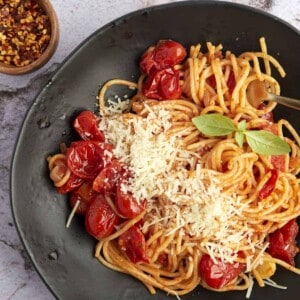 a black plate with a serving of one pan spaghetti with roasted tomatoes topped with Parmesan cheese