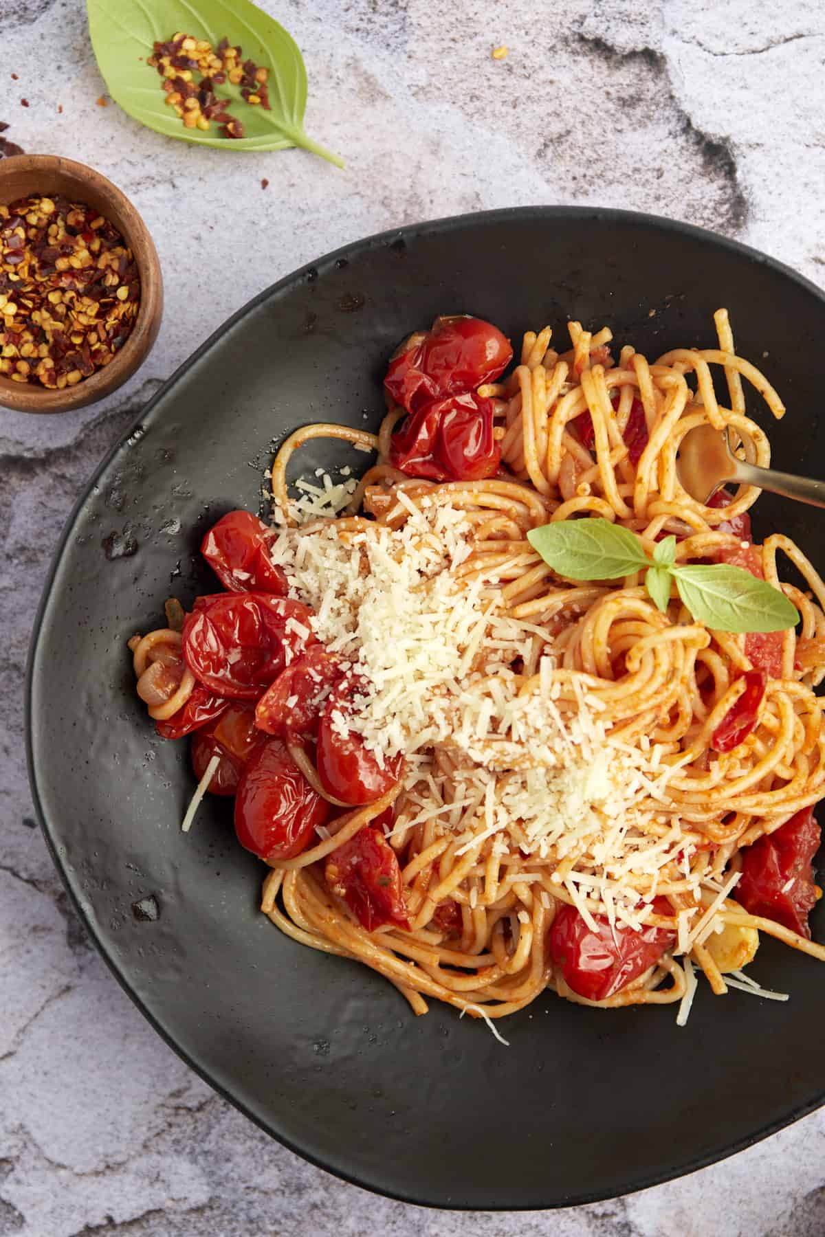 a black plate full of easy one pan spaghetti with roasted tomatoes topped with parmesan cheese