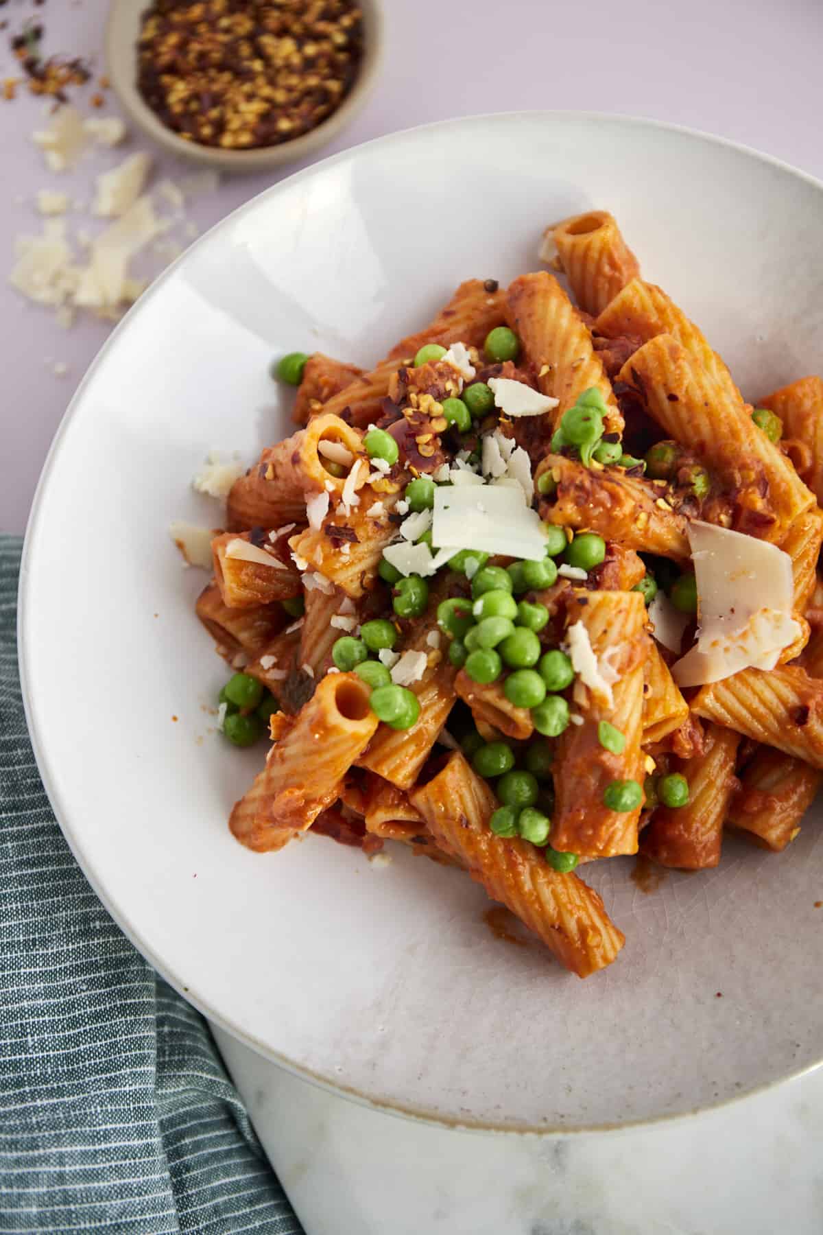 a plate full of spicy baked rigatoni with peas topped with shaved cheese