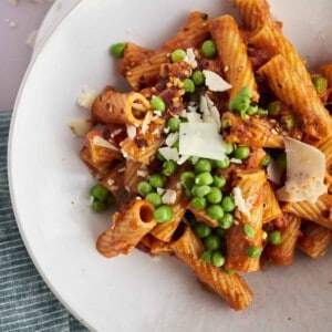 a bowl of spicy baked rigatoni with peas topped with shaved Parmesan