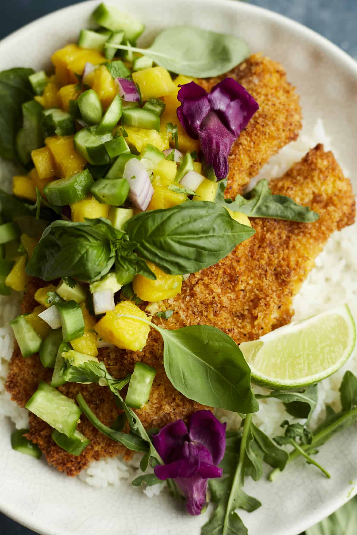 a white plate with a bed of coconut rice, air fried tilapia, and fresh mango salsa