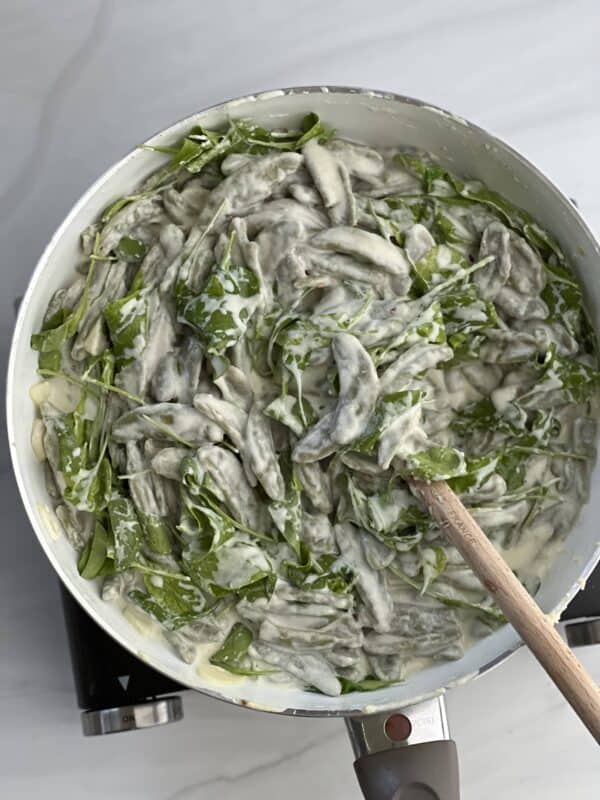 lemon ricotta pasta made with spinach and olive leaf pasta in a pot being stirred with a wooden spoon