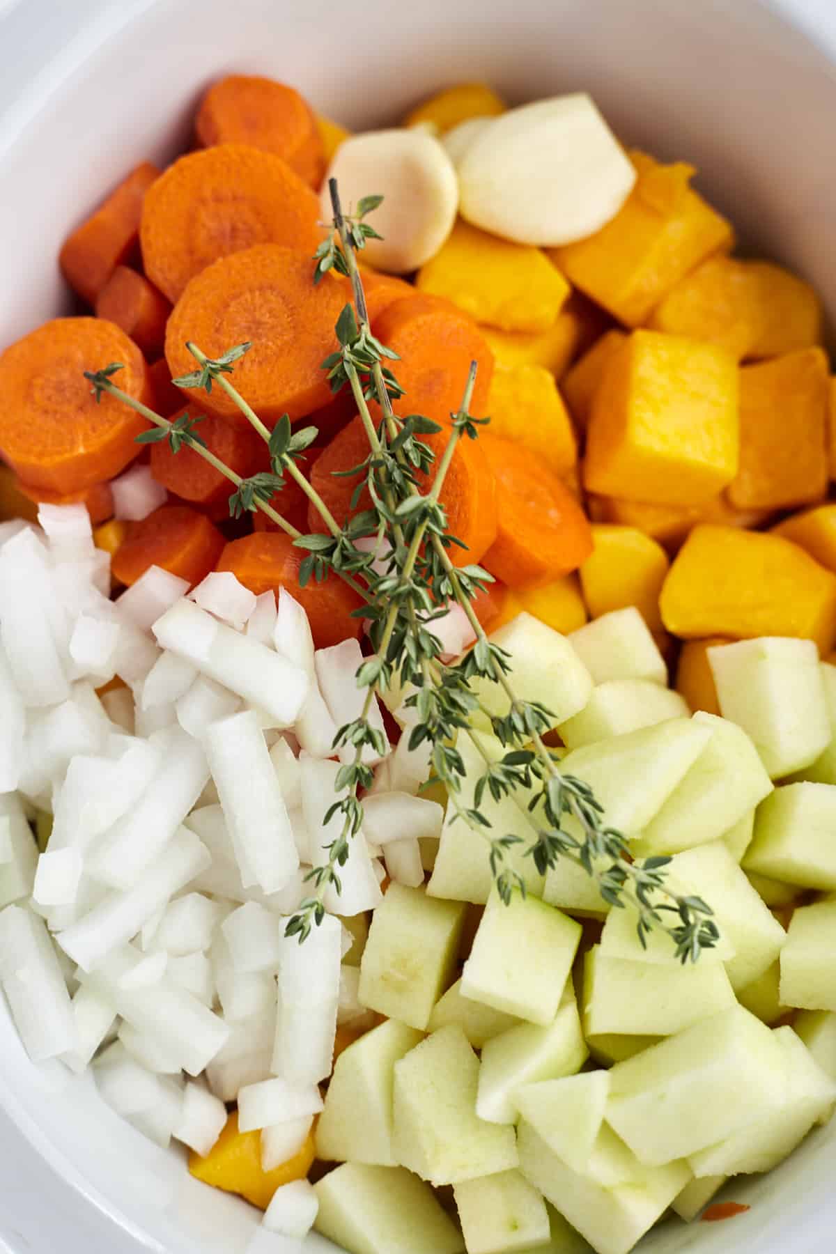 carrots, butternut squash, garlic cloves, diced onion, chopped green apples, and fresh herbs in a slow cooker