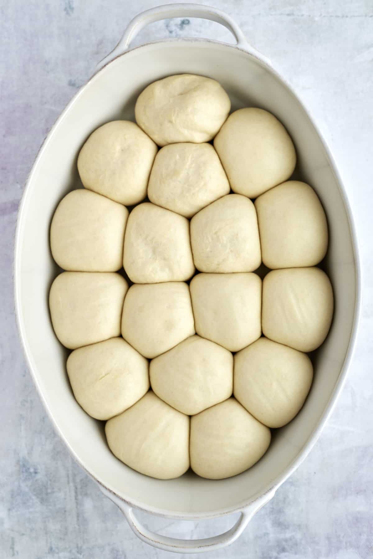 risen unbaked bread rolls in a baking dish