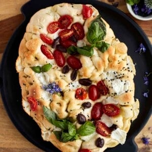 no knead focaccia bread art topped with tomatoes, olives, fresh herbs, and Mozzarell