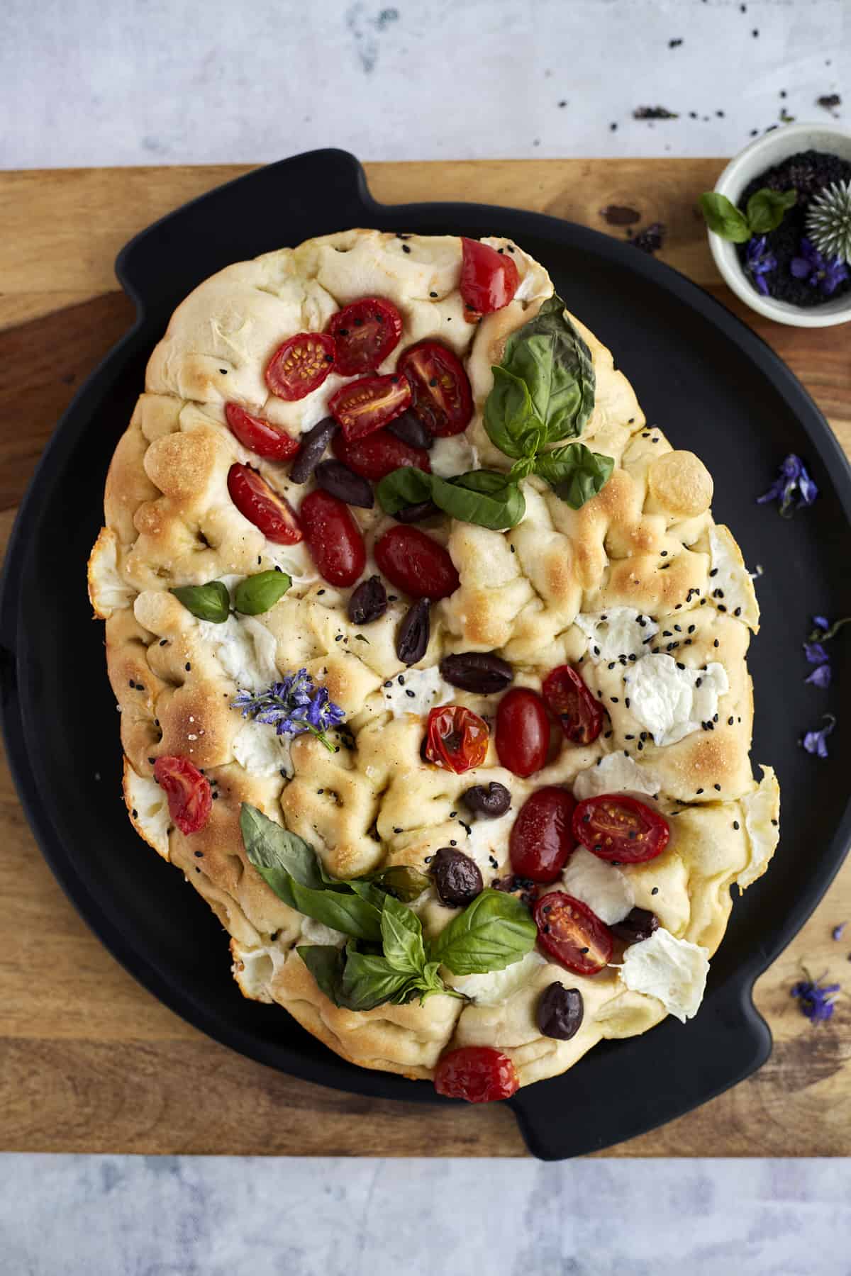 no knead focaccia bread art topped with tomatoes, olives, fresh herbs, and Mozzarell