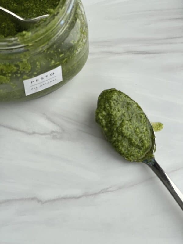a jar of homemade basil pesto with a spoonful of pesto on the side