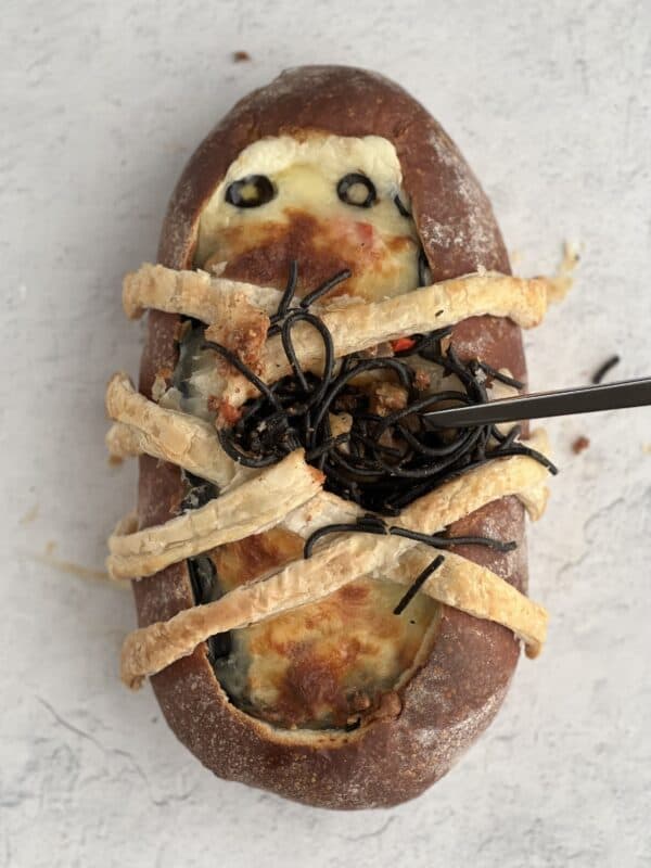 overhead image of a baked mummy spaghetti bread bowl with squid ink pasta bursting out of the center