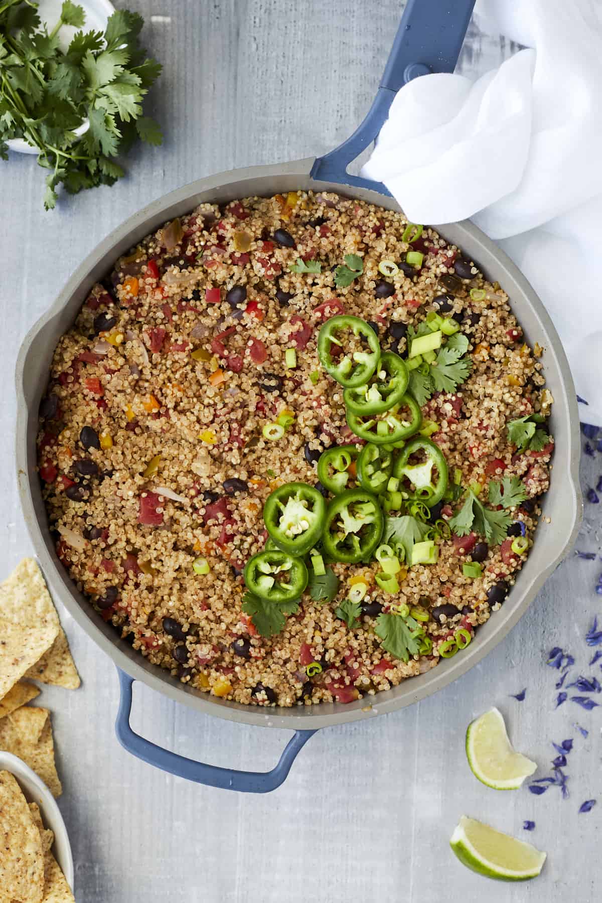 overhead image of a large pot full of Mexican quinoa with veggies and beans topped with sliced jalapenos and cilantro