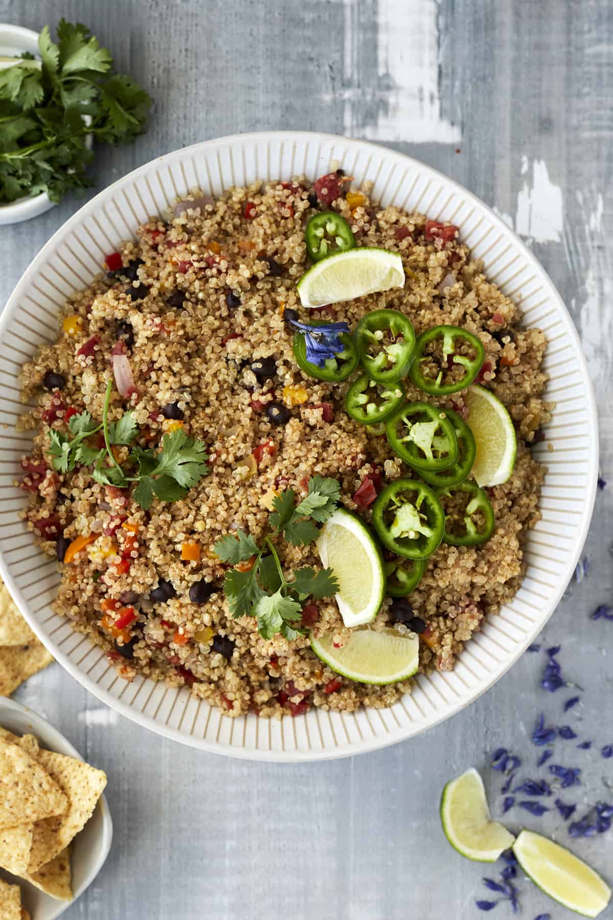 a large white bowl full of Mexican quinoa with veggies and black beans topped with jalapenos, lime wedges, and cilantro
