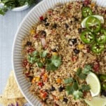 close up image of a white bowl of Mexican quinoa topped with cilantro, lime wedges, and jalapenos