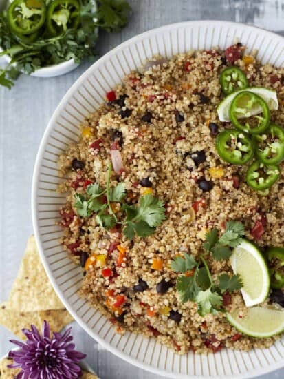 close up image of a white bowl of Mexican quinoa topped with cilantro, lime wedges, and jalapenos