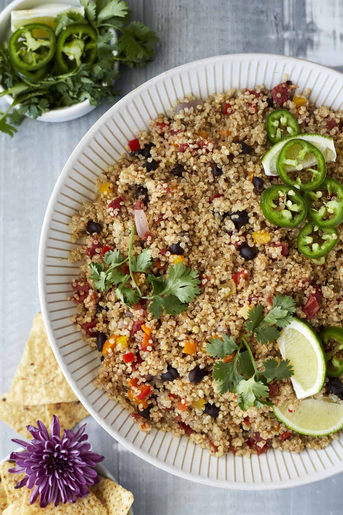 overhead image of a white bowl of Mexican quinoa topped with sliced jalapenos, lime wedges, and fresh cilantro