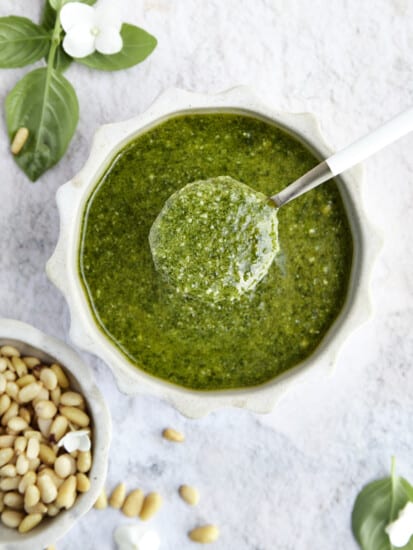 Overhead image of a spoon lifting up a scoop of homemade basil pesto from a bowl.