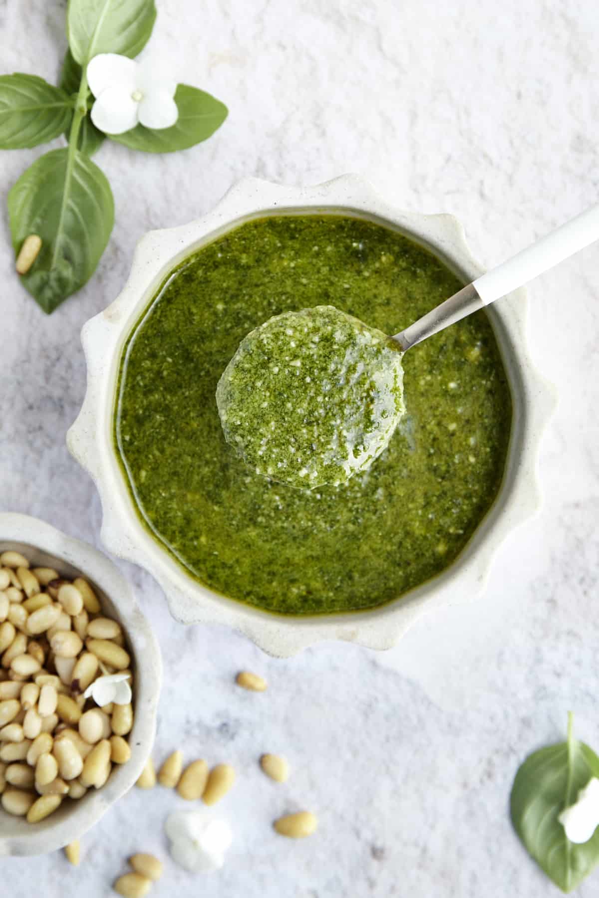 A bowl of basil pesto with a spoon lifting up a scoop. 