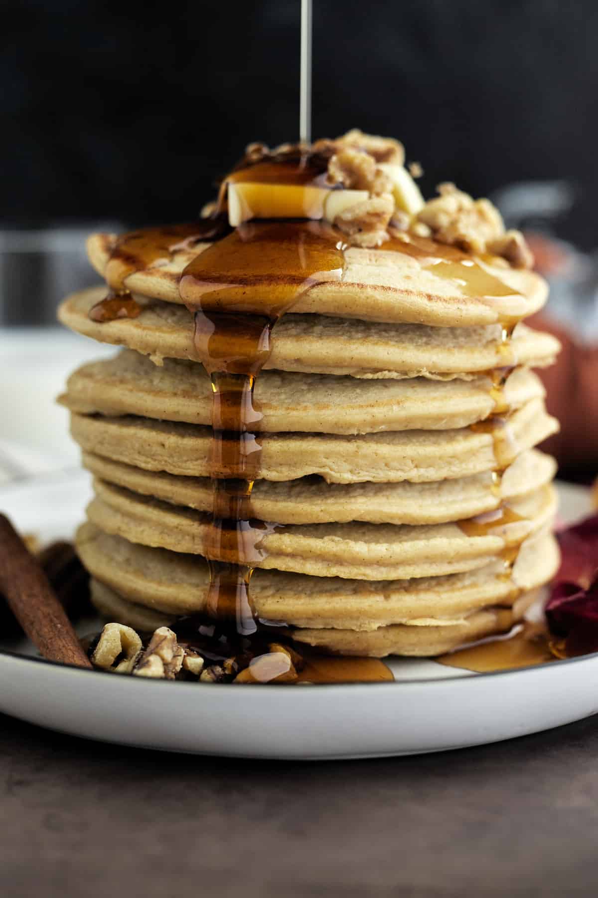 a stack of healthy pumpkin pancakes topped with butter and walnuts with maple syrup drizzled on top