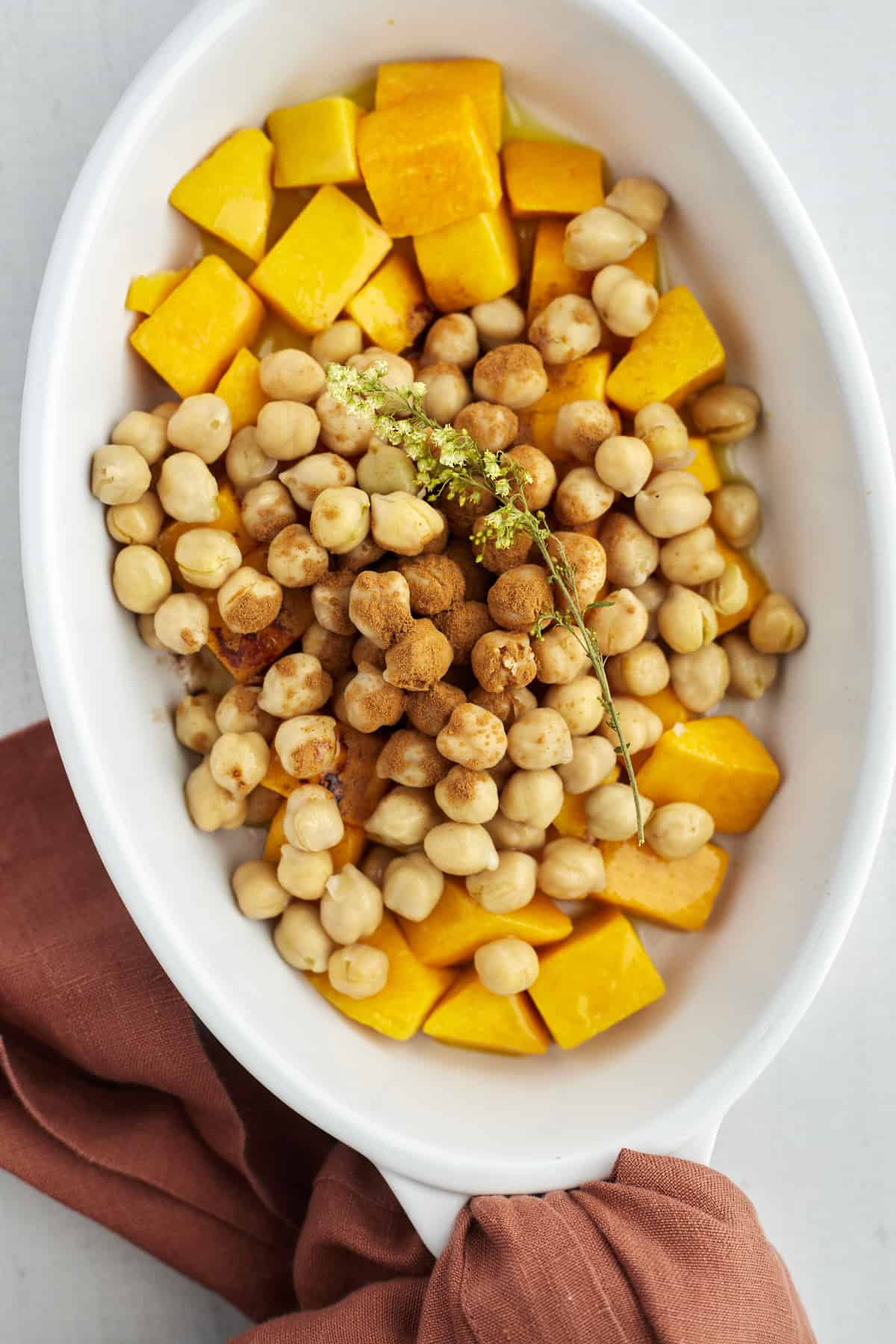 cubed butternut squash and chickpeas in an oval baking dish topped with cinnamon 