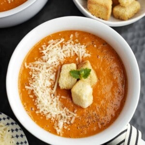 a white bowl full of roasted tomato soup topped with Parmesan cheese and homemade croutons