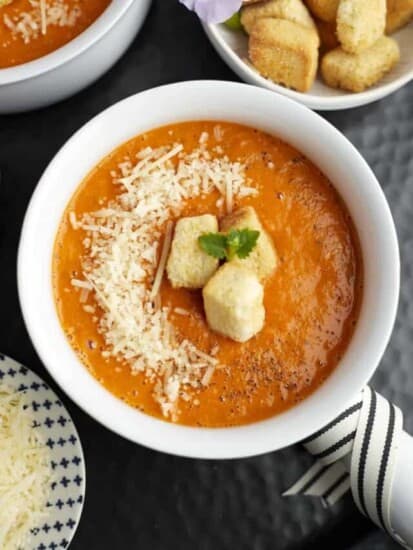 a white bowl full of roasted tomato soup topped with Parmesan cheese and homemade croutons