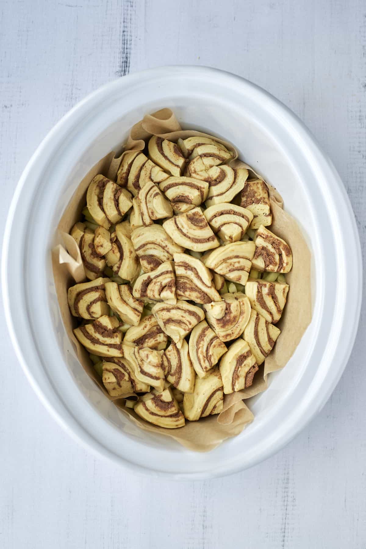 a slow cooker full of unbaked cinnamon roll pieces and apples.