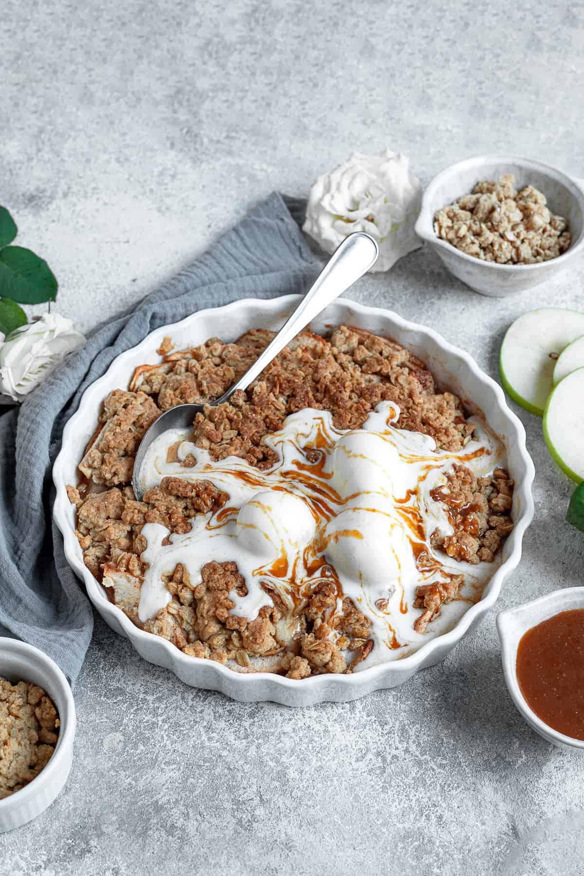 an apple crisp topped with three scoops of melting vanilla ice cream with a spoon stuck in the center