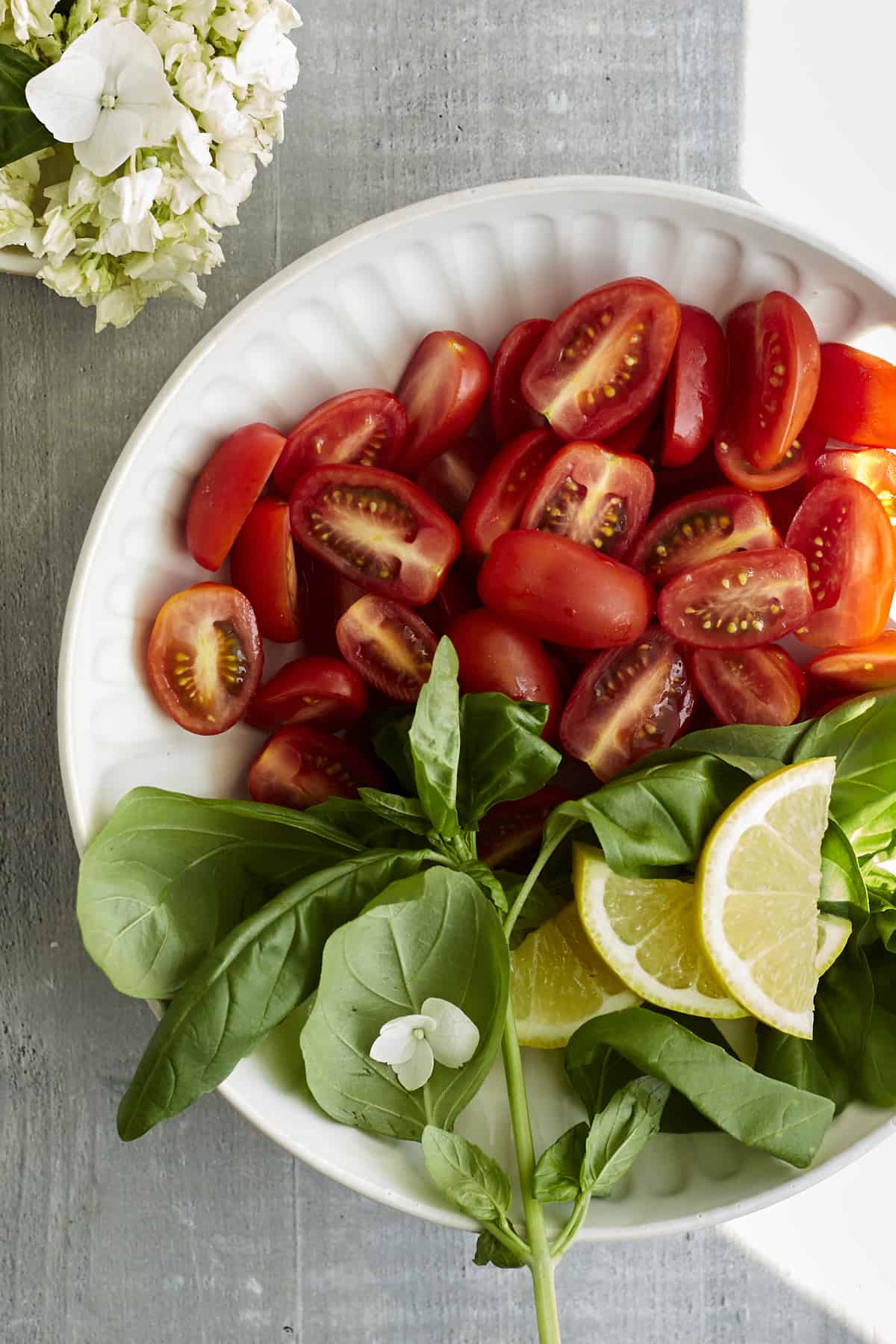 a white plate with halved cherry tomatoes, fresh basil, and lemon wedges