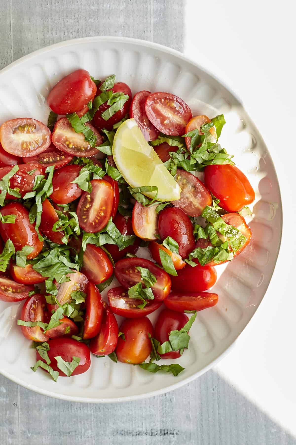 a plate of halved cherry tomatoes topped with fresh basil strips and a lemon wedge