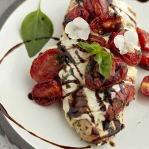 a close up image of baked bruschetta chicken topped with mozzarella, tomatoes, balsamic vinegar, and basil