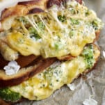 two roasted garlic and broccoli oven grilled cheese sandwiches on top of each other with the filling oozing out.