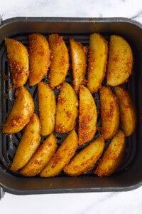 Raw seasoned potato wedges in an air fryer.