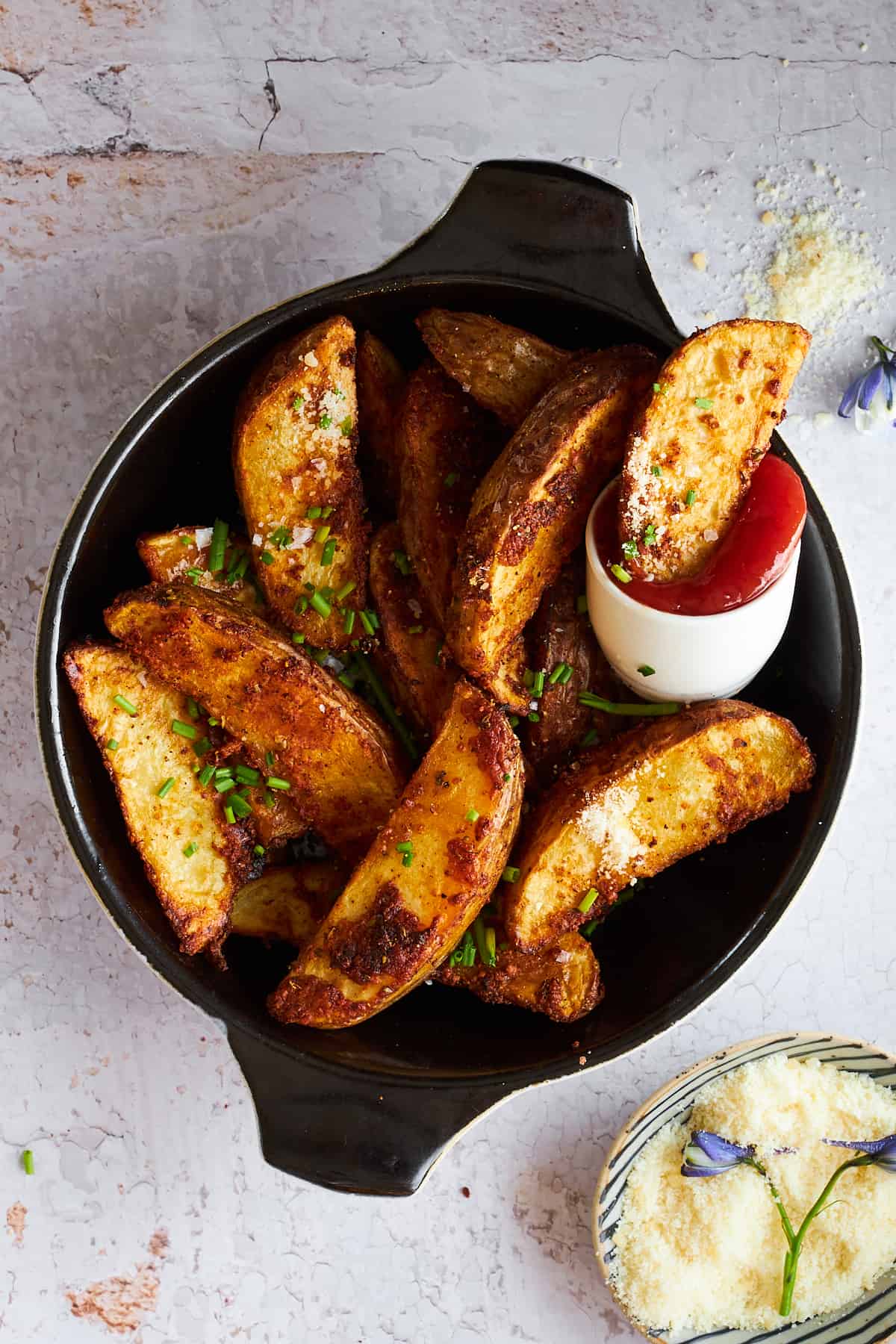 Garlic parmesan potato wedges in a bowl with a small bowl of ketchup. 