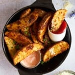 Garlic parmesan potato wedges on a plate with dipping sauces.