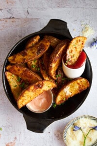 Garlic parmesan potato wedges on a plate with dipping sauces.