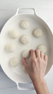 a hand placing raw dough balls in an oval baking dish 