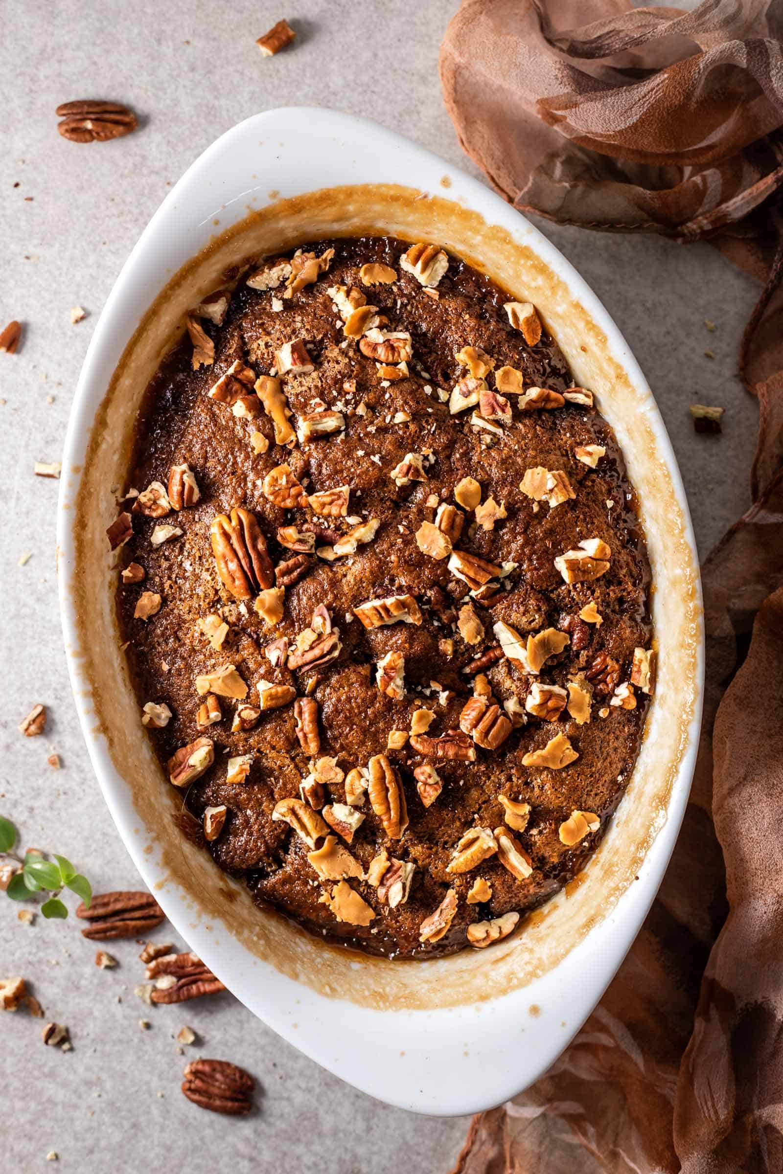 overhead image of easy pecan pie cobbler in an oval baking dish topped with chopped pecans 