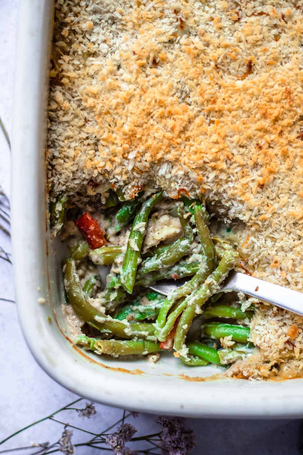 cheesy green bean casserole in a baking dish with a spoon scooping out a serving.