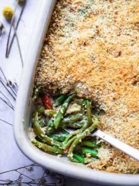 a baking dish of cheesy green bean casserole with a serving scooped out of the bottom lefthand corner.