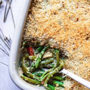 a baking dish of cheesy green bean casserole with a serving scooped out of the bottom lefthand corner