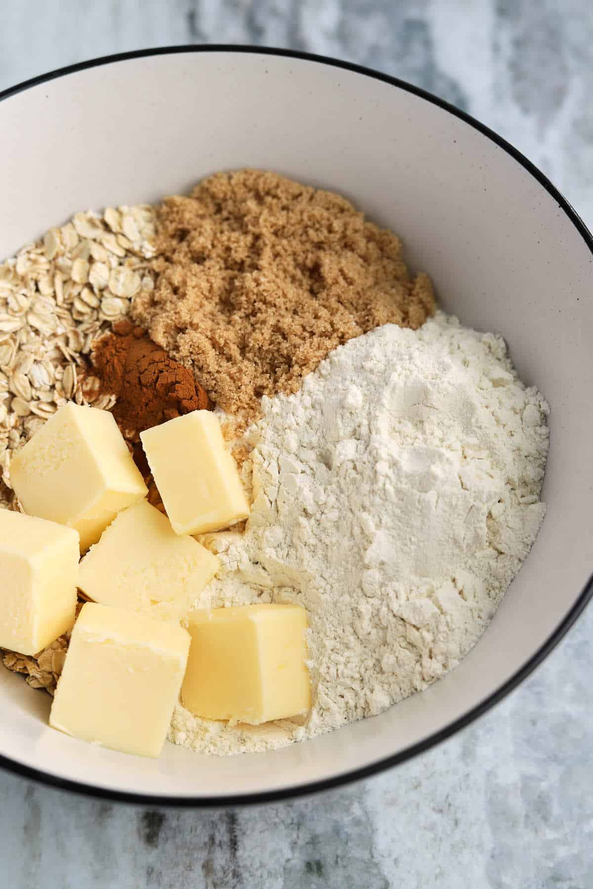 bowl of oat crumble ingredients with cold butter, flour, brown sugar, oats, and cinnamon